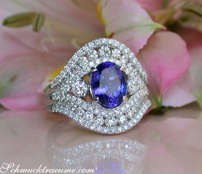 Weißgoldring mit Tansanit und Diamanten, Detailaufnahme, sanfte Formen, rosa Blüten im Hintergrund Weißgoldring mit Tansanit und Diamanten, Detailaufnahme, sanfte Formen, rosa Blüten im Hintergrund