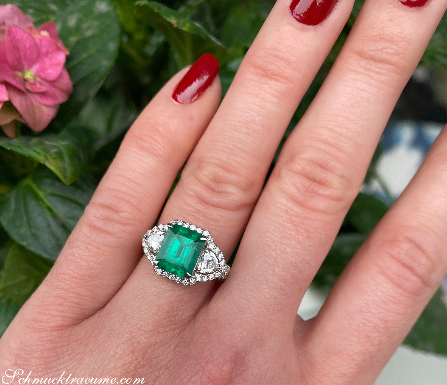 Detailansicht von Smaragd-Ring mit Diamanten in Weißgold, vor Blütenhintergrund.