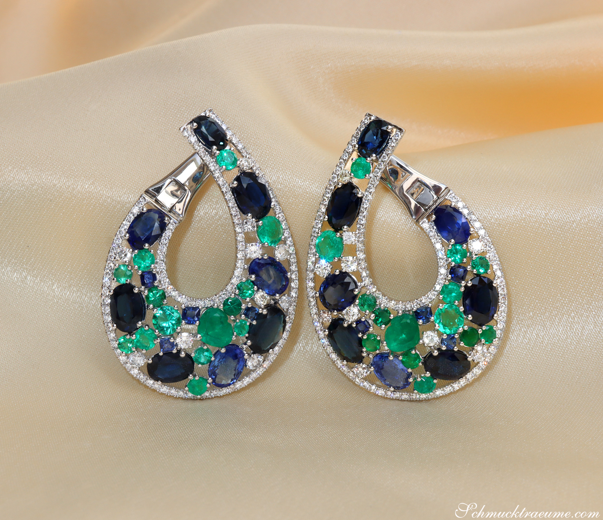 Detail der Luxus-Ohrgehänge mit Saphiren, Smaragden und Brillanten auf cremefarbenem Stoff