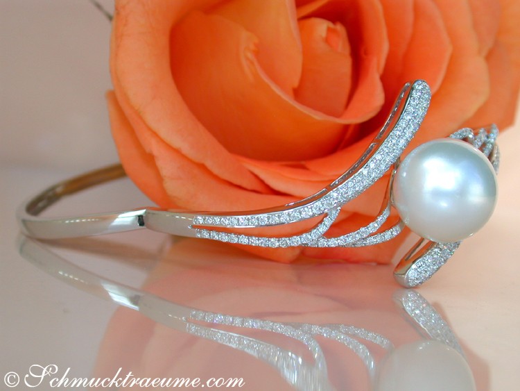 Weißgold-Armreif mit Südseeperle, Detailaufnahme, funkelnde Diamanten, rosa Blüte im Hintergrund