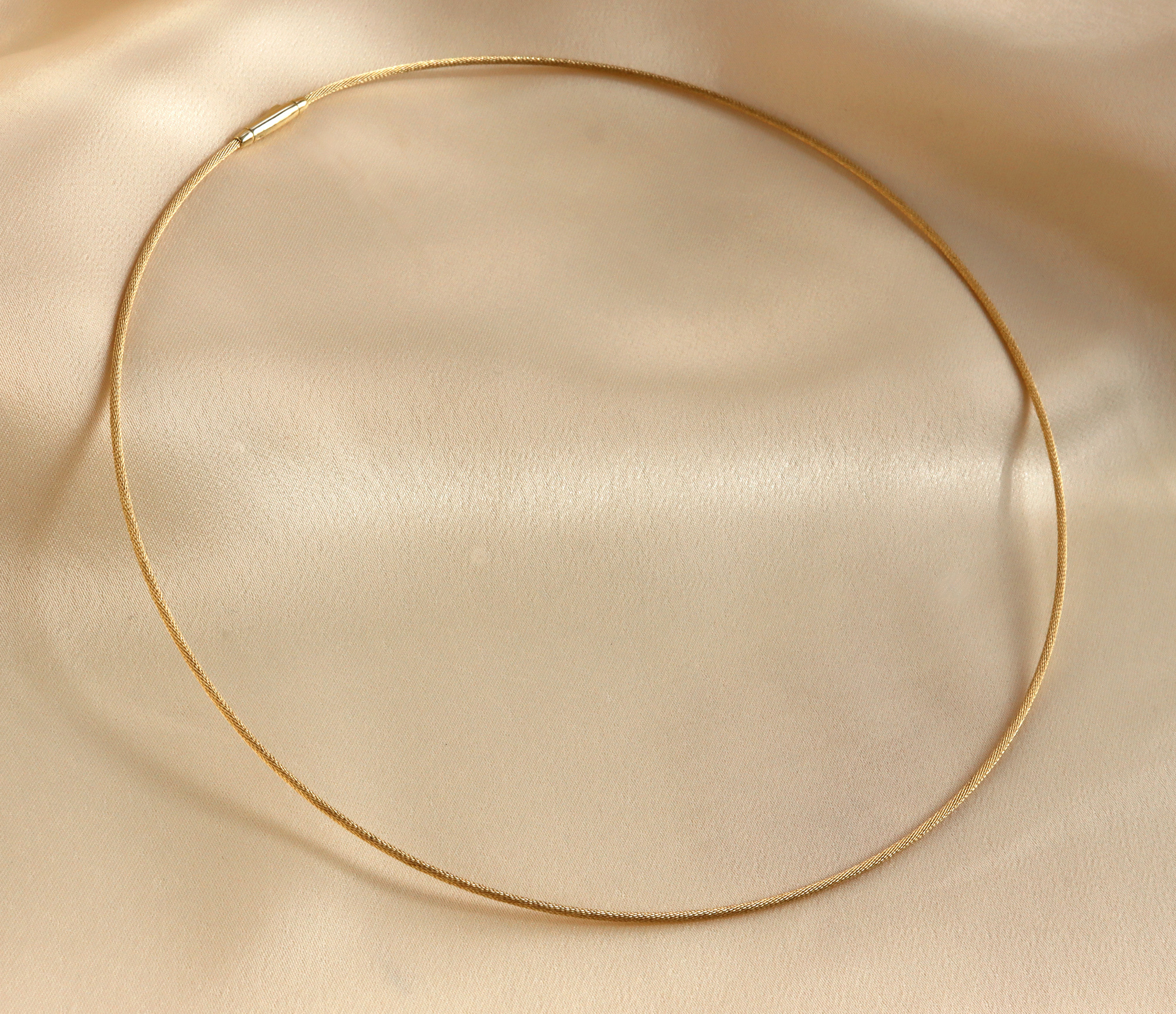 Geflochtener Halsreif aus Gelbgold 750, Detailaufnahme auf cremefarbenem Stoff.