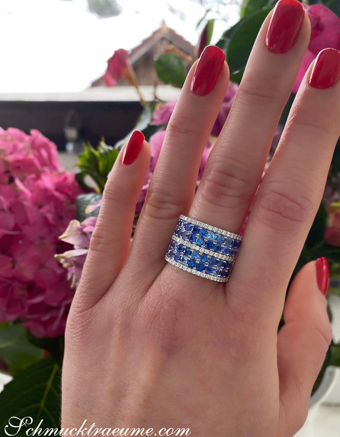 Prächtiger Saphir-Bandring mit Brillanten, roter Nagellack, Blumen im Hintergrund