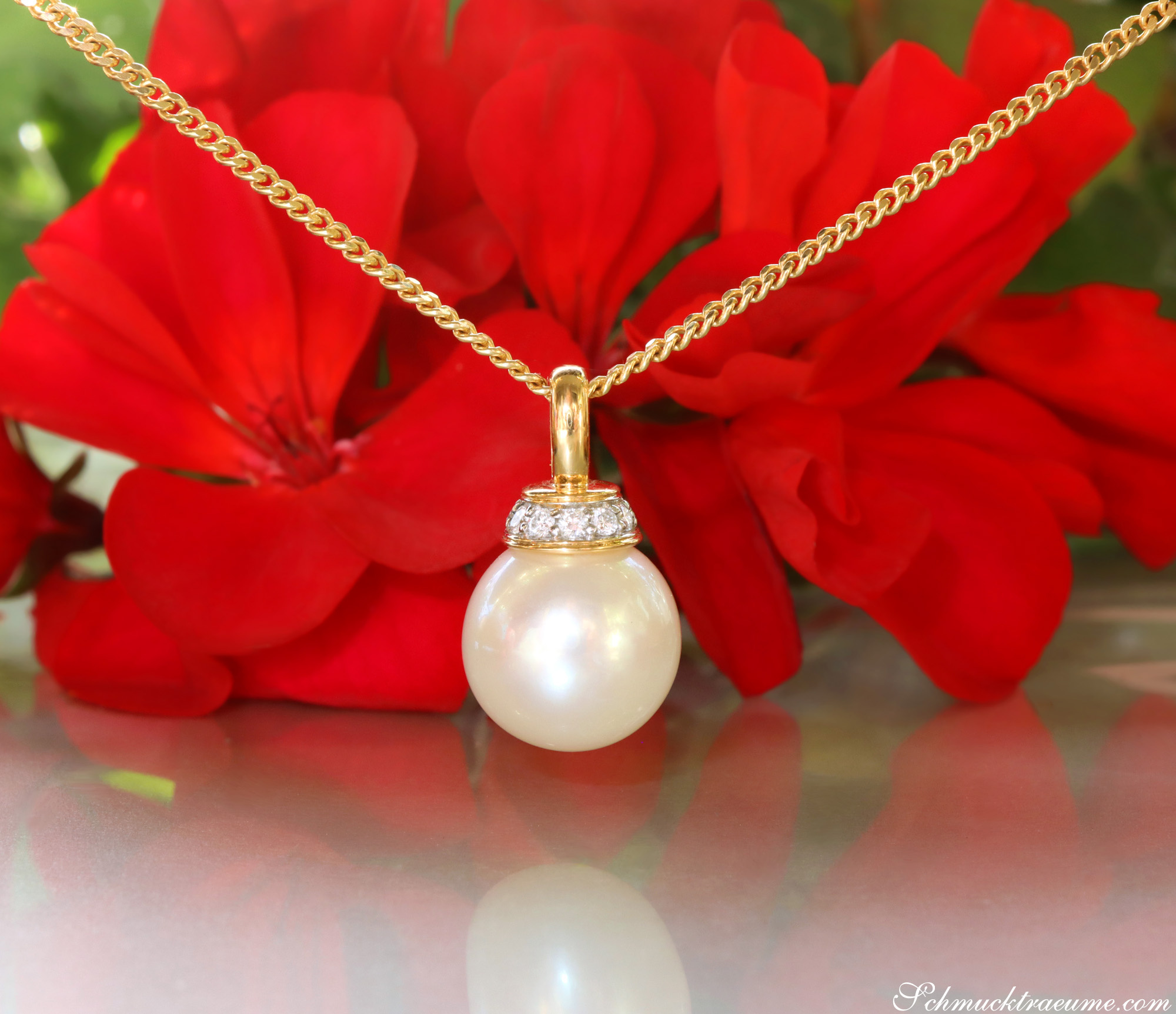 Goldkette mit Süßwasserperlenanhänger und Brillanten, vor roten Blüten.