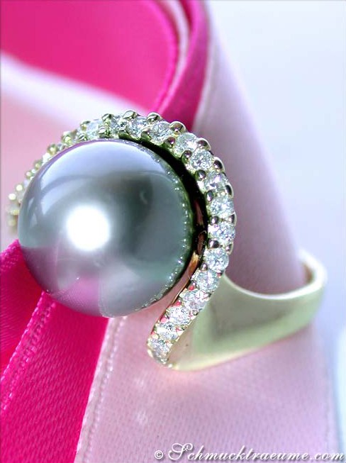 Gelbgoldring mit runder Tahitiperle und Brillanten-Kragen, Detailaufnahme auf pinker Schleife.