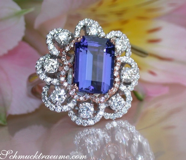 Smaragdschliff-Tanzanit-Ring mit Diamanten in Roségold 750, Detailaufnahme, Blumen im Hintergrund Smaragdschliff-Tanzanit-Ring mit Diamanten in Roségold 750, Detailaufnahme, Blumen im Hintergrund