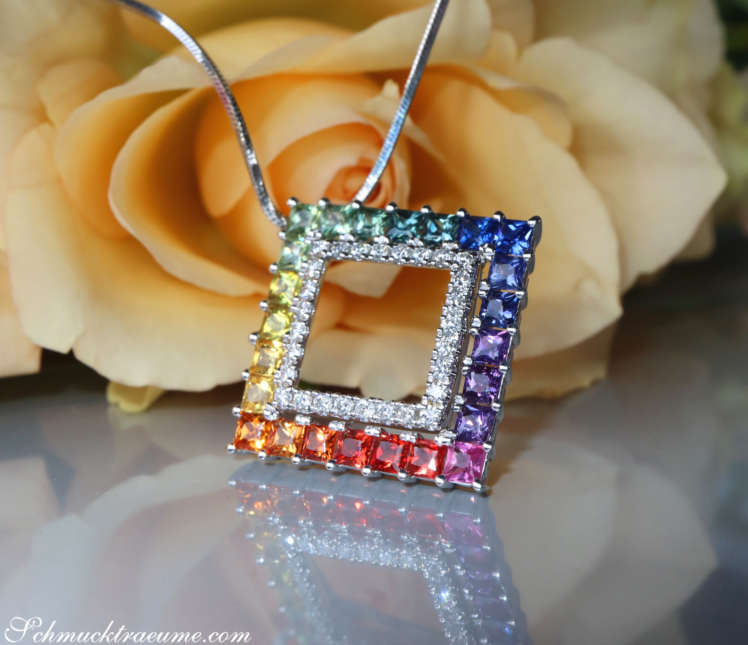 Weißgold-Anhänger mit Regenbogen-Saphiren und Brillanten, detailreich, vor Rosenblüte.