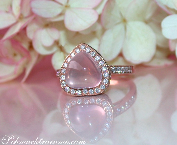 Rosenquarz Herz Ring mit Diamanten auf rosa Blütenhintergrund
