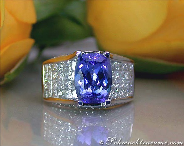 Goldener Tansanit-Ring mit Prinzessinnen- und Brillantschliff, blauviolett, umgeben von Diamanten, vor gelben Rosenblüten.