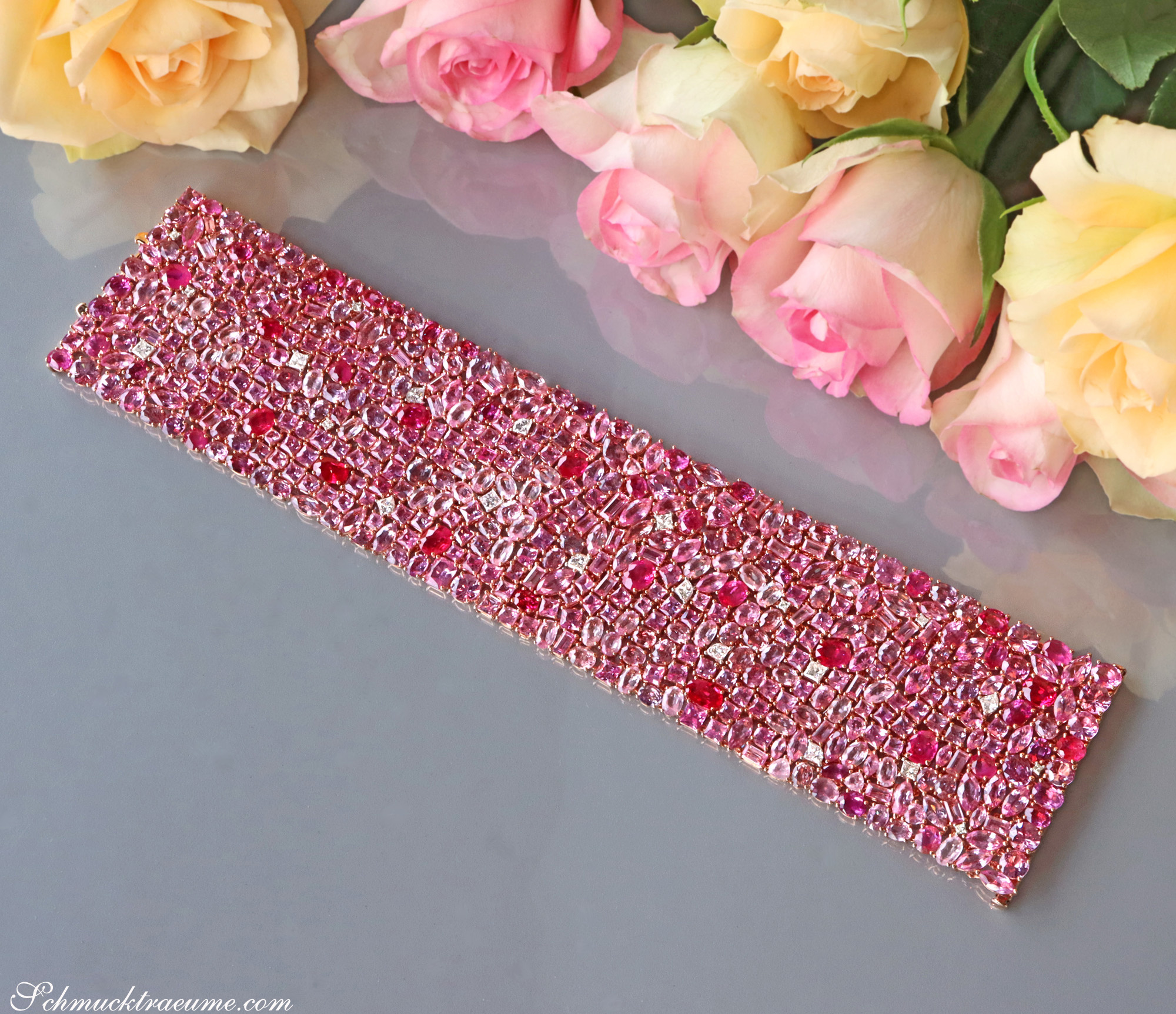 Rosa Saphir-Armband mit 485 Steinen, 115,07 ct., auf glänzender Oberfläche, umgeben von Rosenblüten.