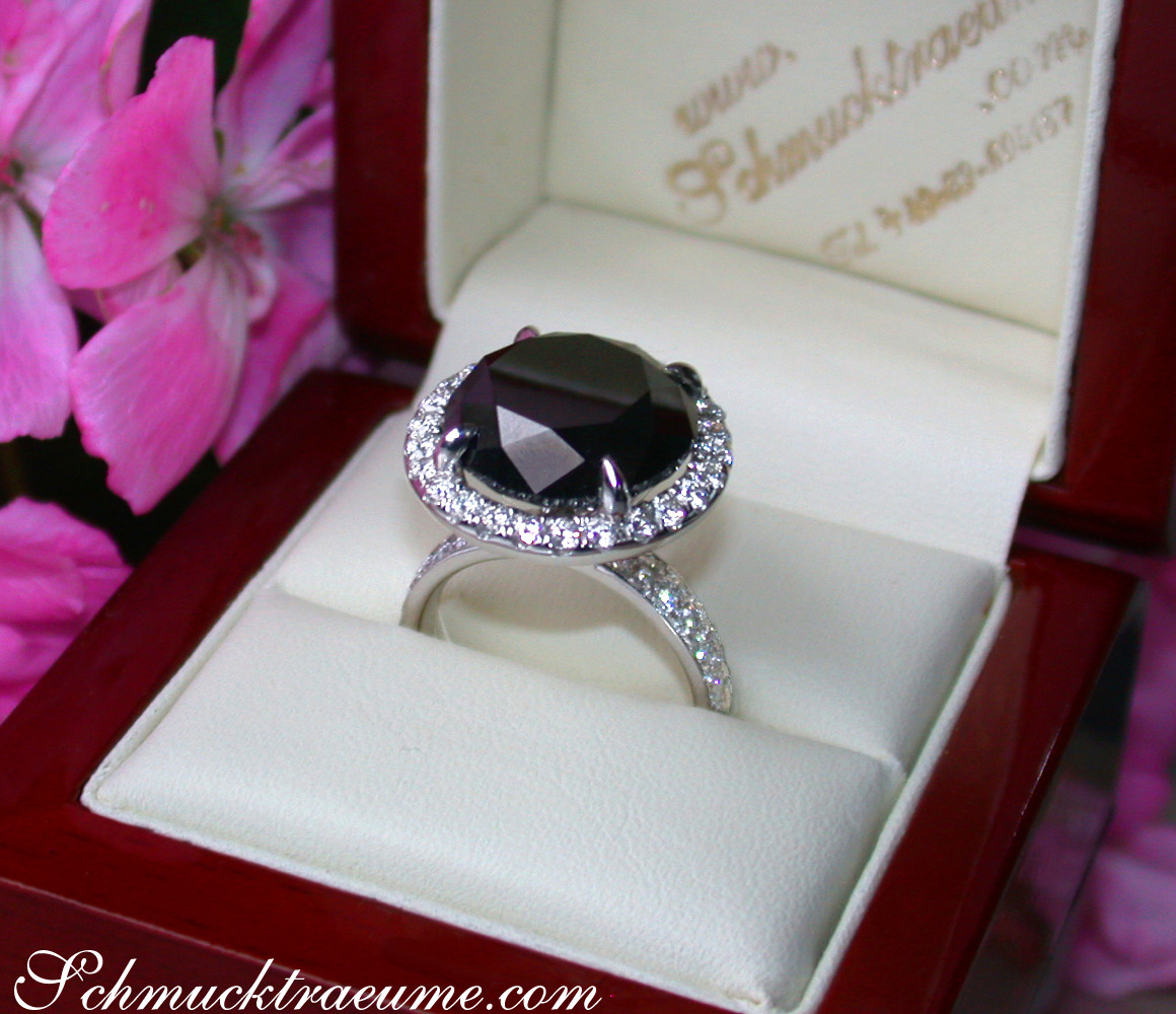 Schwarzdiamant-Solitär-Ring in Weißgold, umgeben von Brillanten, im Box-Set, vor Blüten.