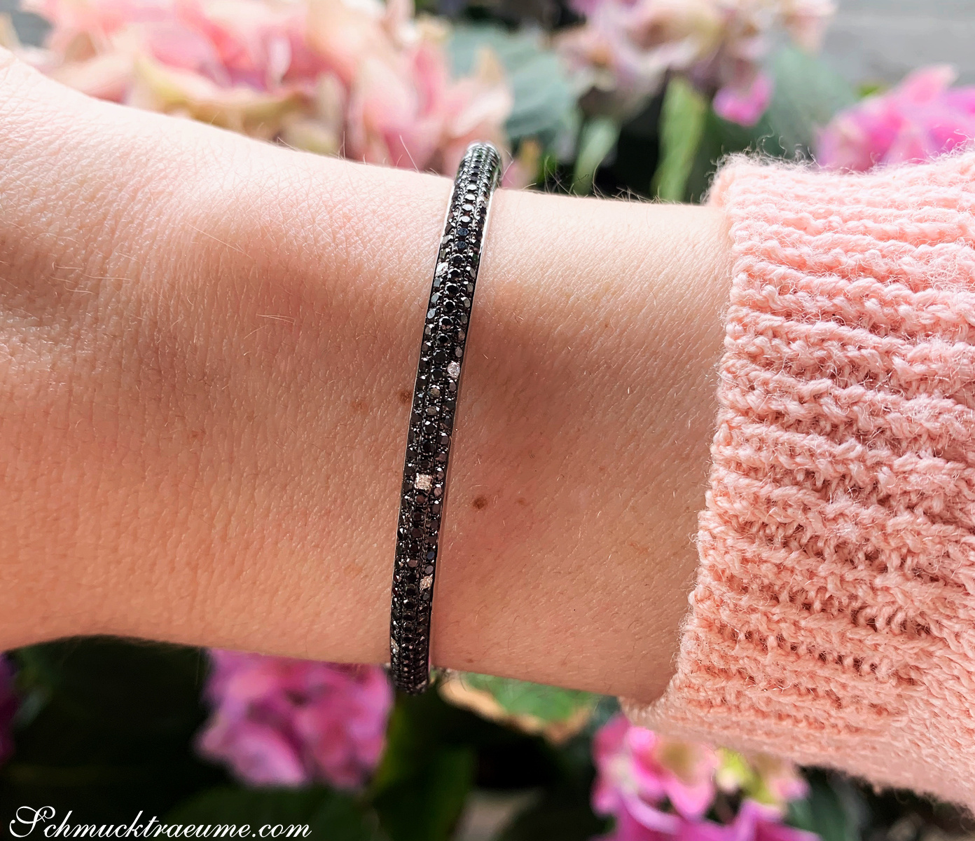 Armband mit schwarzen Diamanten auf Hand mit rosa Pullover, Detailaufnahme
