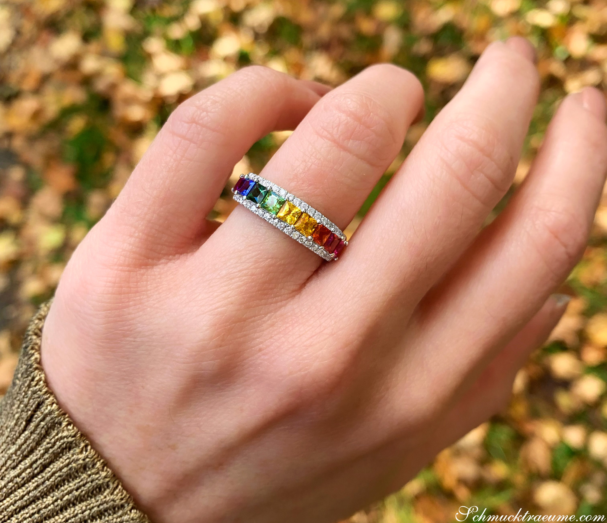 Regenbogen-Saphir-Ring mit Brillanten auf Hand, Herbstblätter im Hintergrund