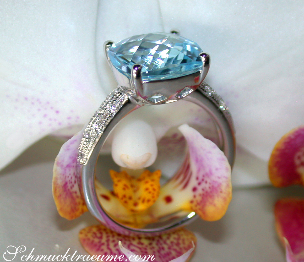 Weißgoldring mit Blautopas und Diamanten, Detailaufnahme mit Orchideenblüte im Hintergrund