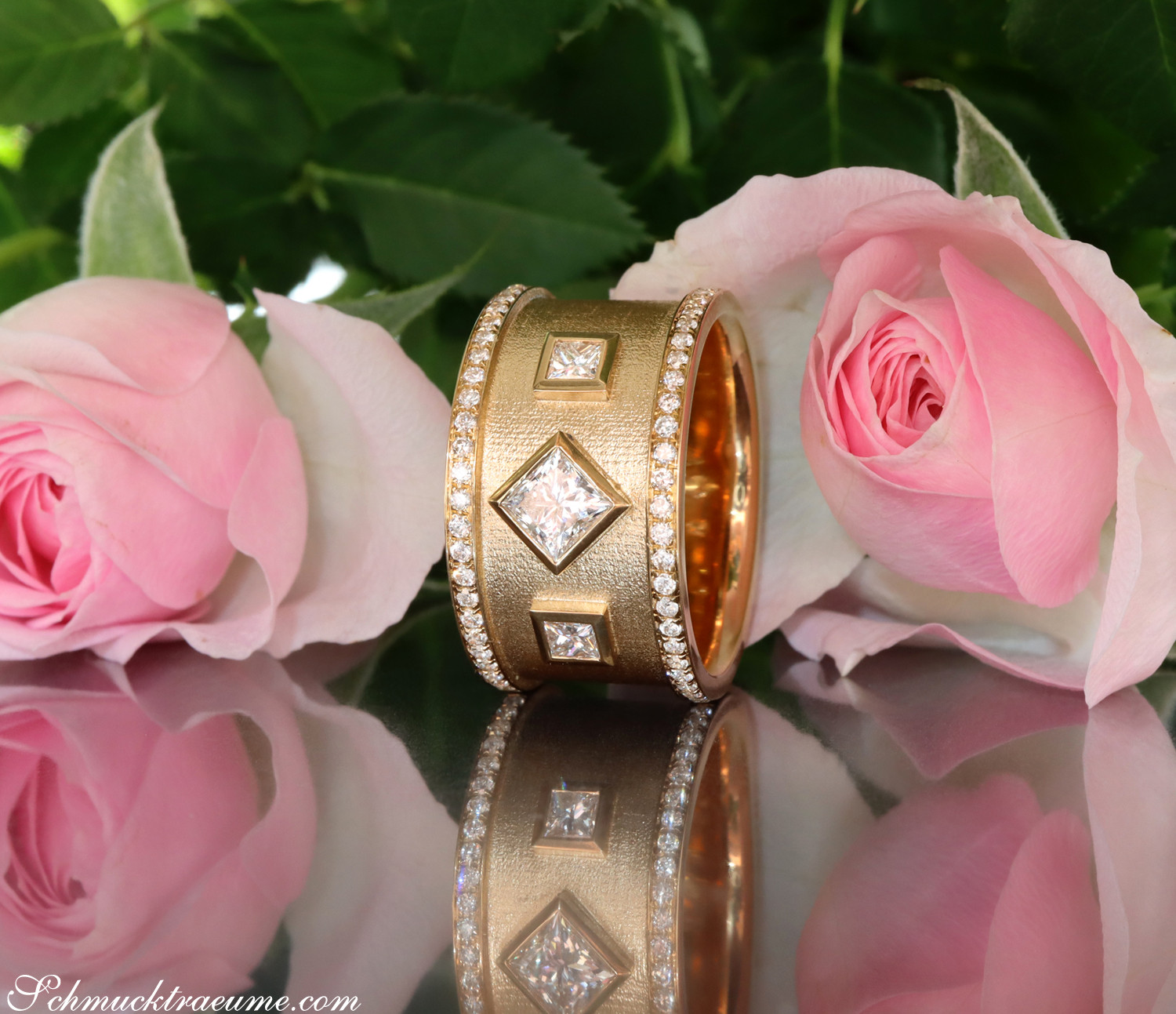 Goldener Diamant-Ring mit Princess-Diamanten und Diamant-Saum, Rosen im Hintergrund.