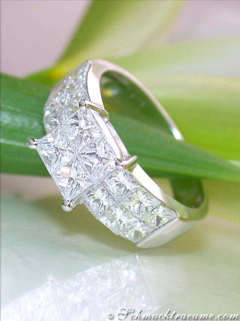 Detailansicht des eleganten Princess-Diamant-Rings, klarer Weißgoldschmuck, scharfe Linien, auf grünem Blatt liegend