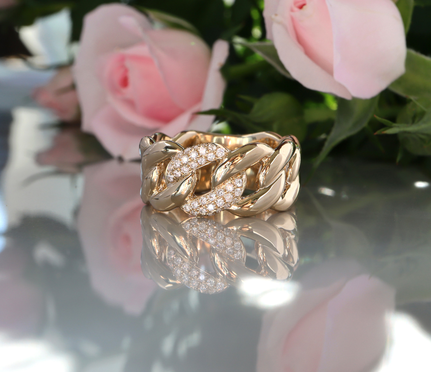 Goldener Panzerkettenring mit Brillanten, Rosen im Hintergrund, Detailaufnahme