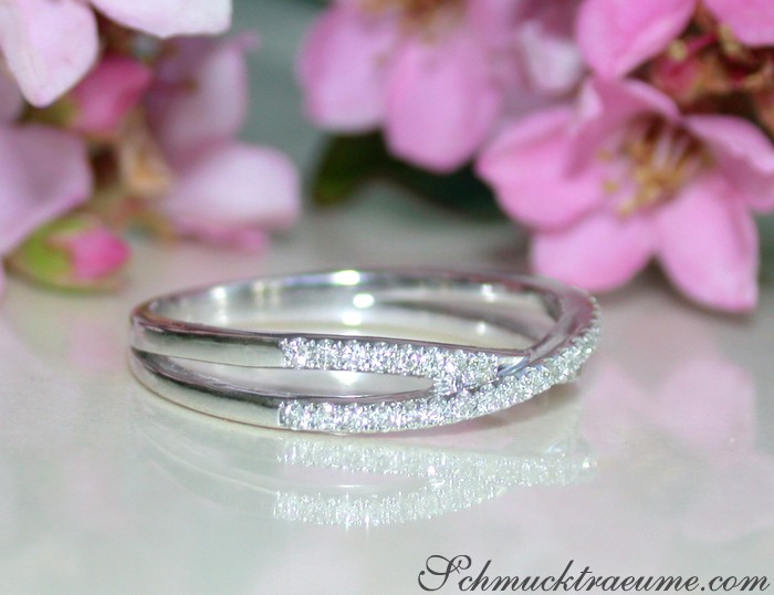 Zarte Diamant-Ring mit überkreuzten Strängen, elegant auf weißem Untergrund mit Kirschblüten im Hintergrund.