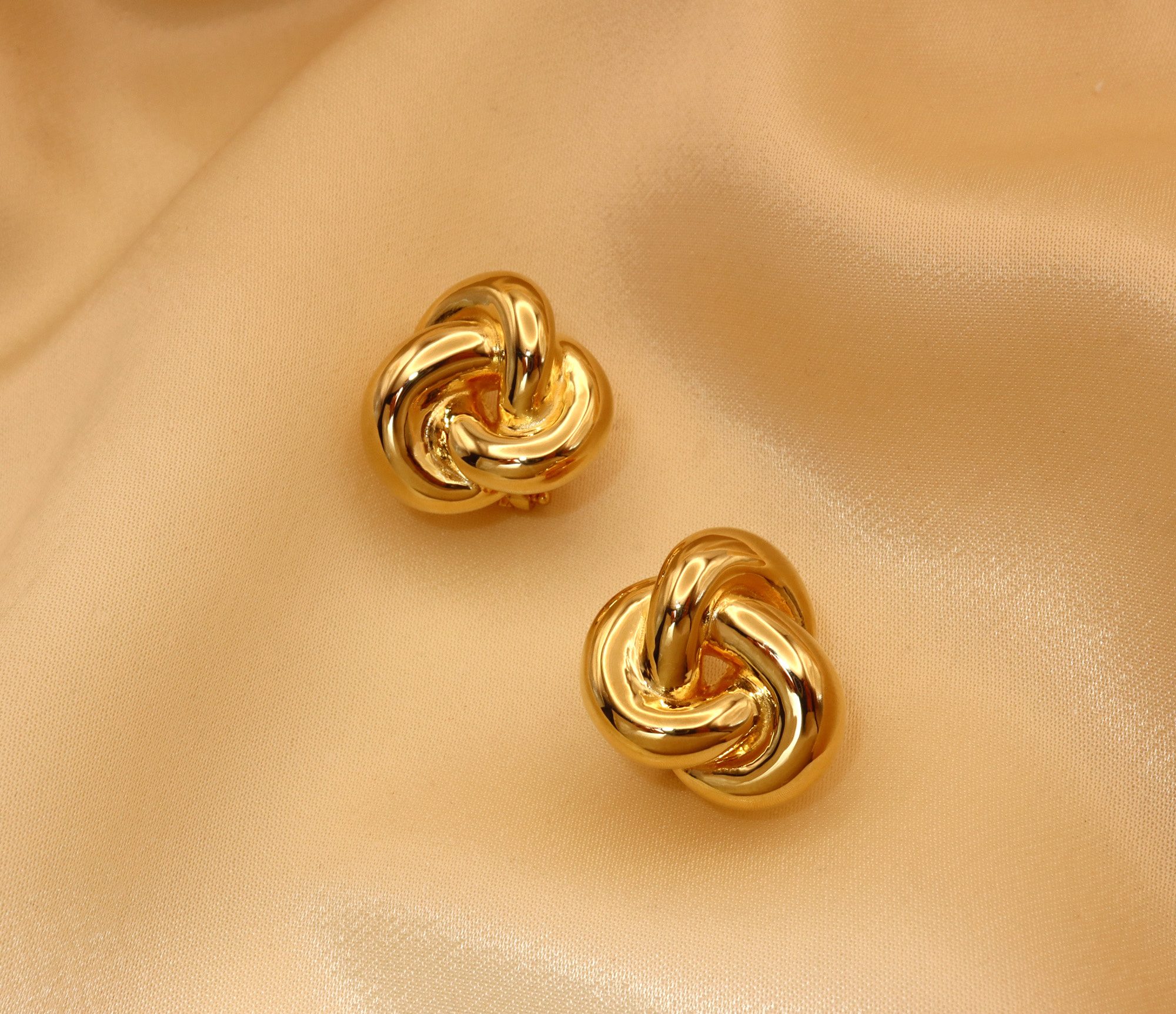 Goldene Knoten Ohrstecker aus 585er Gelbgold auf sattem Stoff, Detailaufnahme.