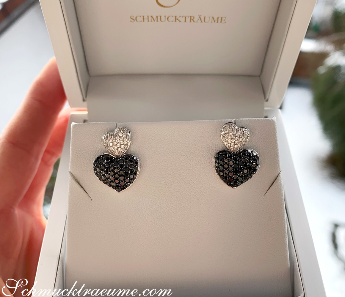 Ohrstecker mit Herzform in Weißgold, schwarzen und weißen Diamanten, präsentiert in Schmuckschachtel.