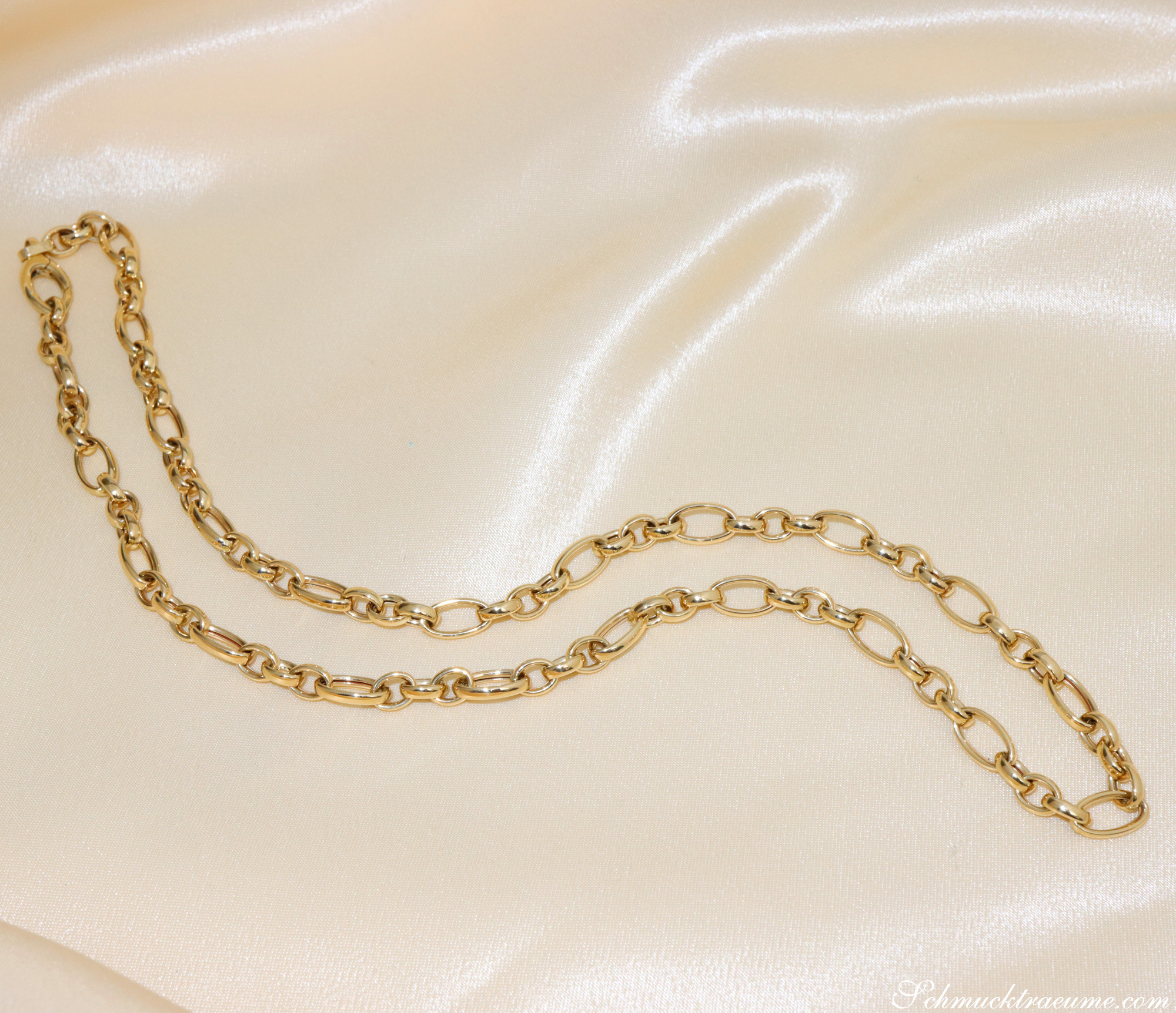 Goldene Halskette aus ovalen und runden Gliedern auf cremefarbenem Stoff.