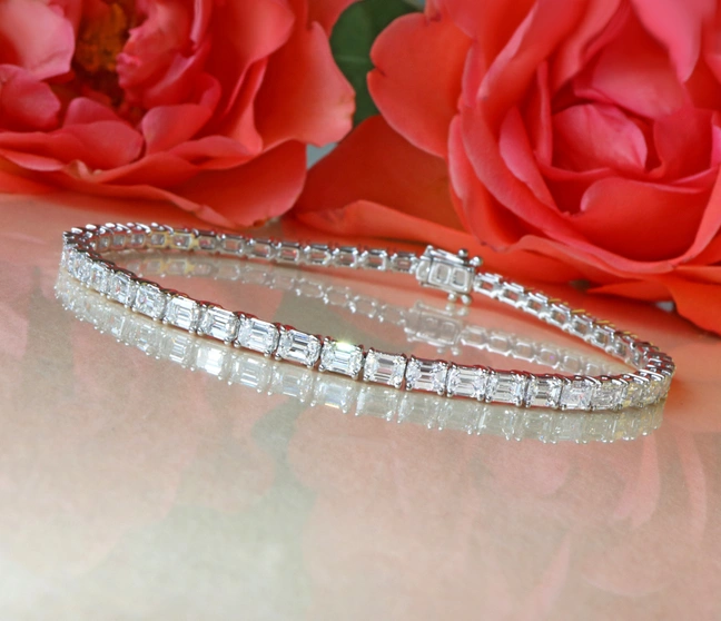 Diamant-Tennisarmband im Smaragdschliff auf rosa Hintergrund mit Rosenblüten. Diamant-Tennisarmband im Smaragdschliff auf rosa Hintergrund mit Rosenblüten.