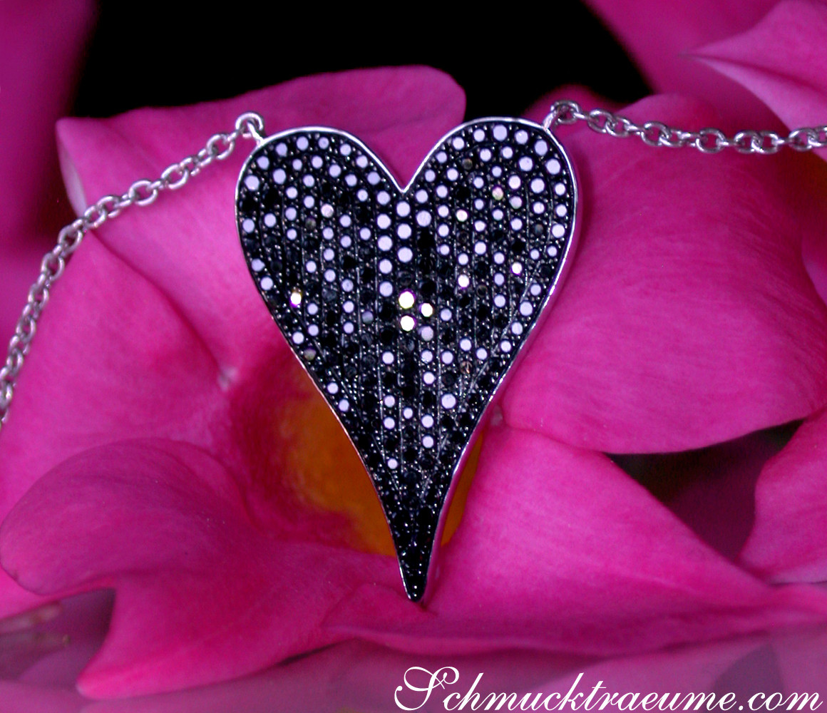 Herzanhänger mit schwarzen Diamanten auf rosa Blüte, Detailaufnahme.