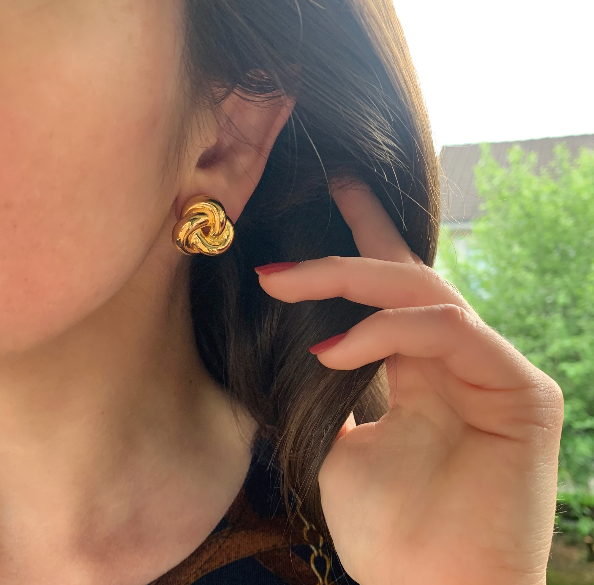 Goldene Knoten-Ohrstecker im Gelbgold 585, Detailaufnahme vor grünem Hintergrund