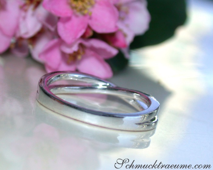 Schmaler Diamant-Ring auf glänzender Oberfläche, Hintergrund mit rosa Blütenblättern