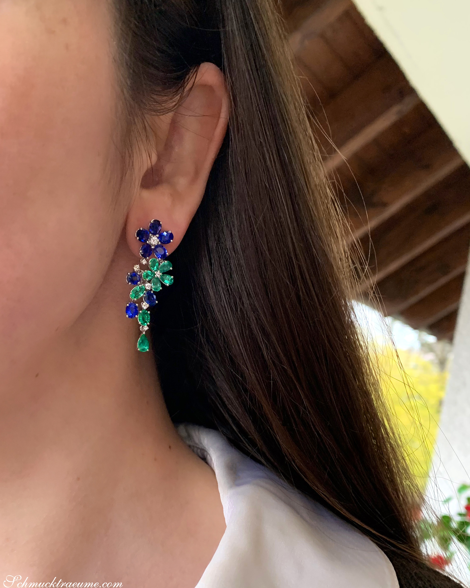 Weibliche Ohren mit prächtigen Smaragd-Saphir-Blumenohrringen, Detailaufnahme.