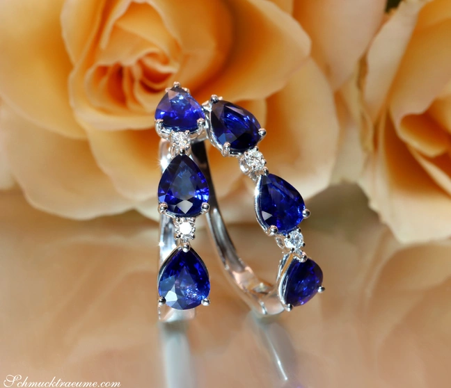 Blauer Saphir-Tropfen-Ohrstecker mit Diamanten, elegant auf Rosenblüte platziert. Blauer Saphir-Tropfen-Ohrstecker mit Diamanten, elegant auf Rosenblüte platziert.