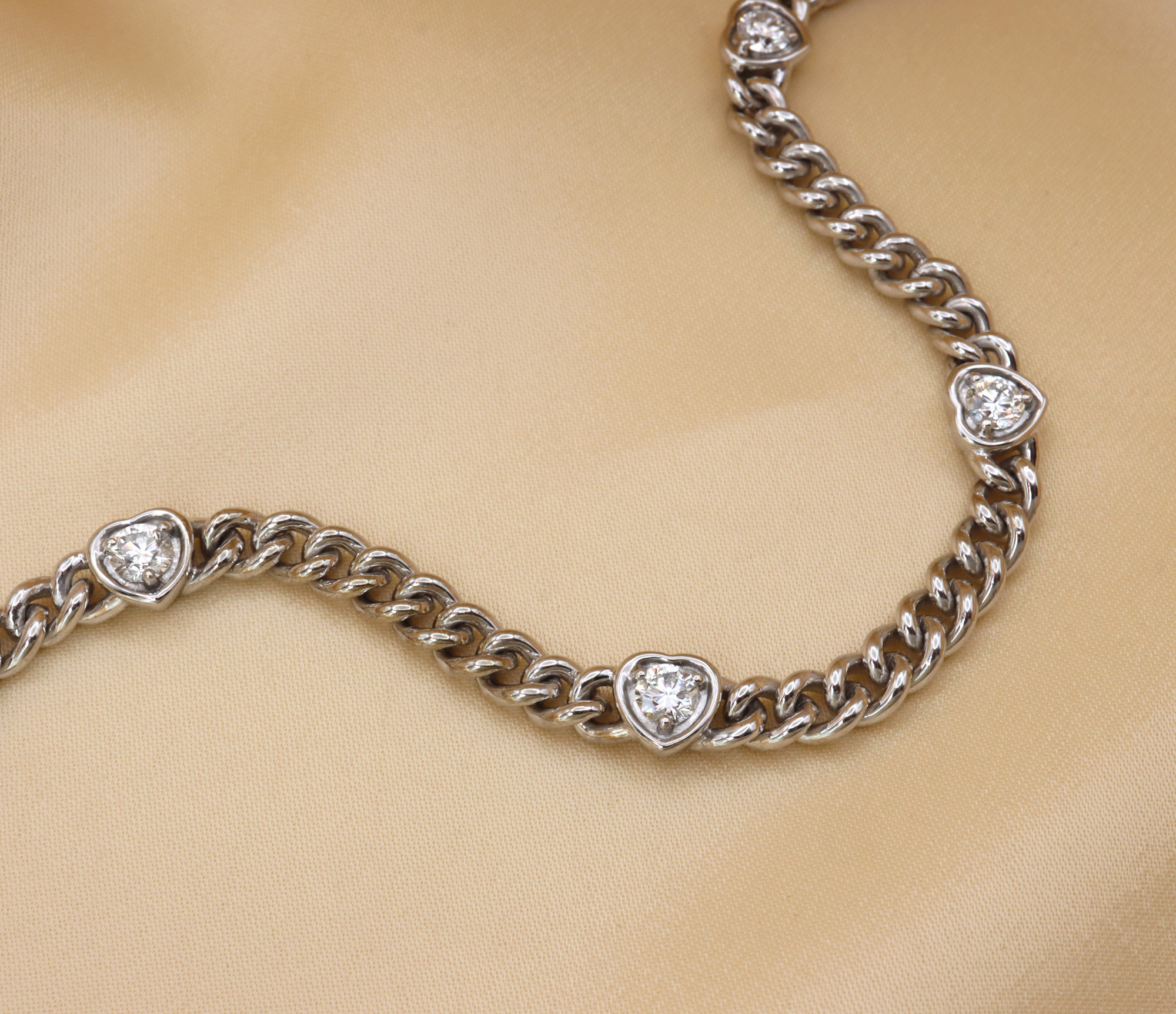 Weiße Goldarmbanddetail mit funkelnden Brillant-Herzen auf cremefarbener Unterlage