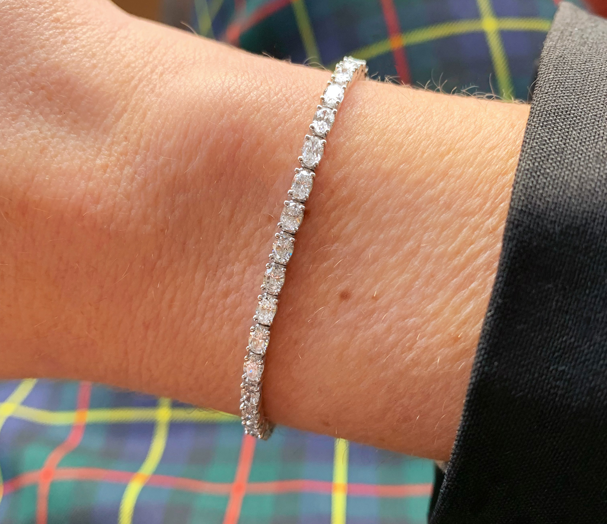 Diamantene Tennisarmband mit Ovalschliff-Diamanten, Detailaufnahme auf der Hand, vor kariertem Hintergrund.