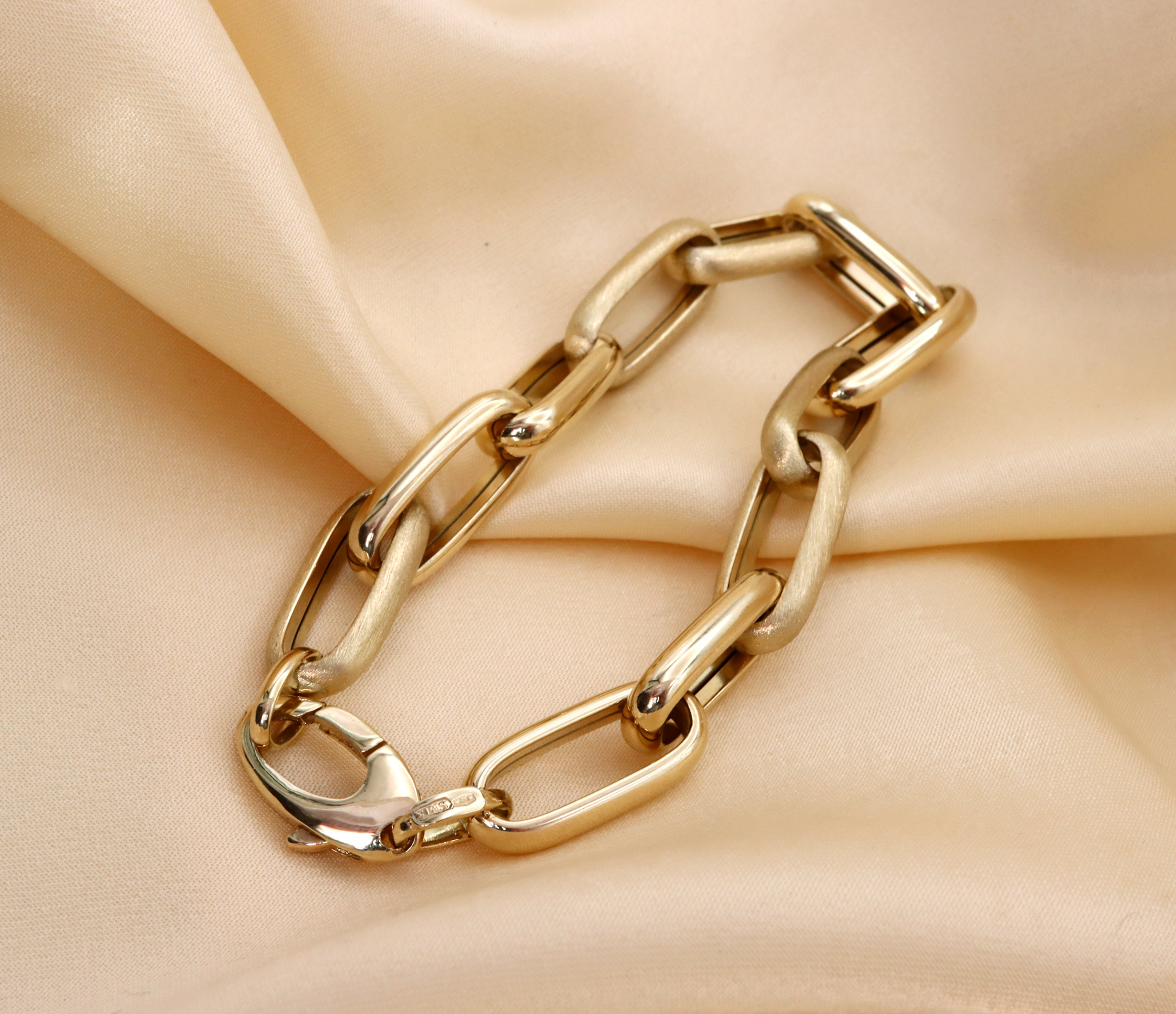 Goldene Paperclip-Armband auf seidigem Stoff, Detailaufnahme, hochglänzend, 585er Gelbgold.