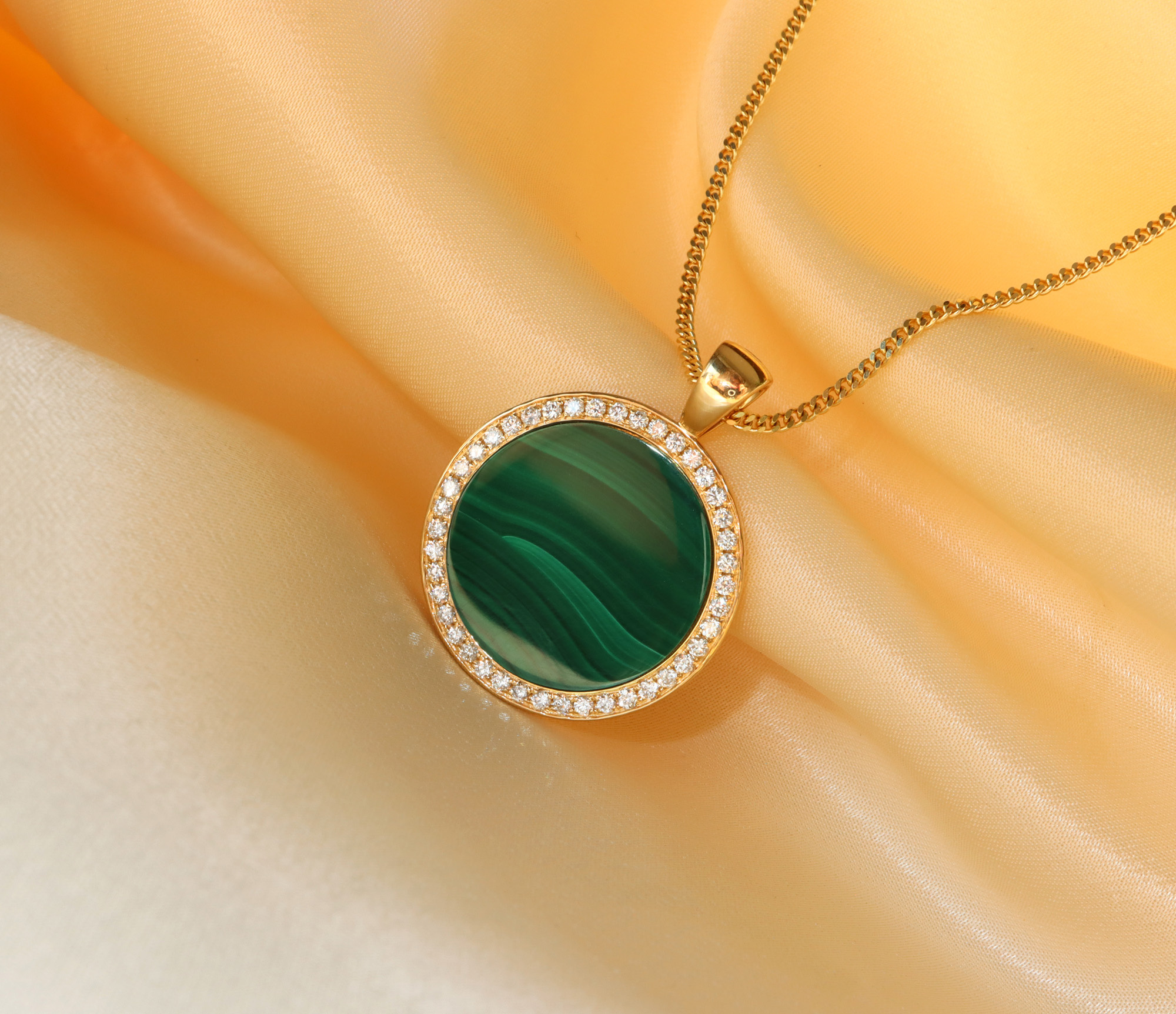 Goldene Kette mit Malachit-Anhänger und Diamanten auf gelbem Tuch