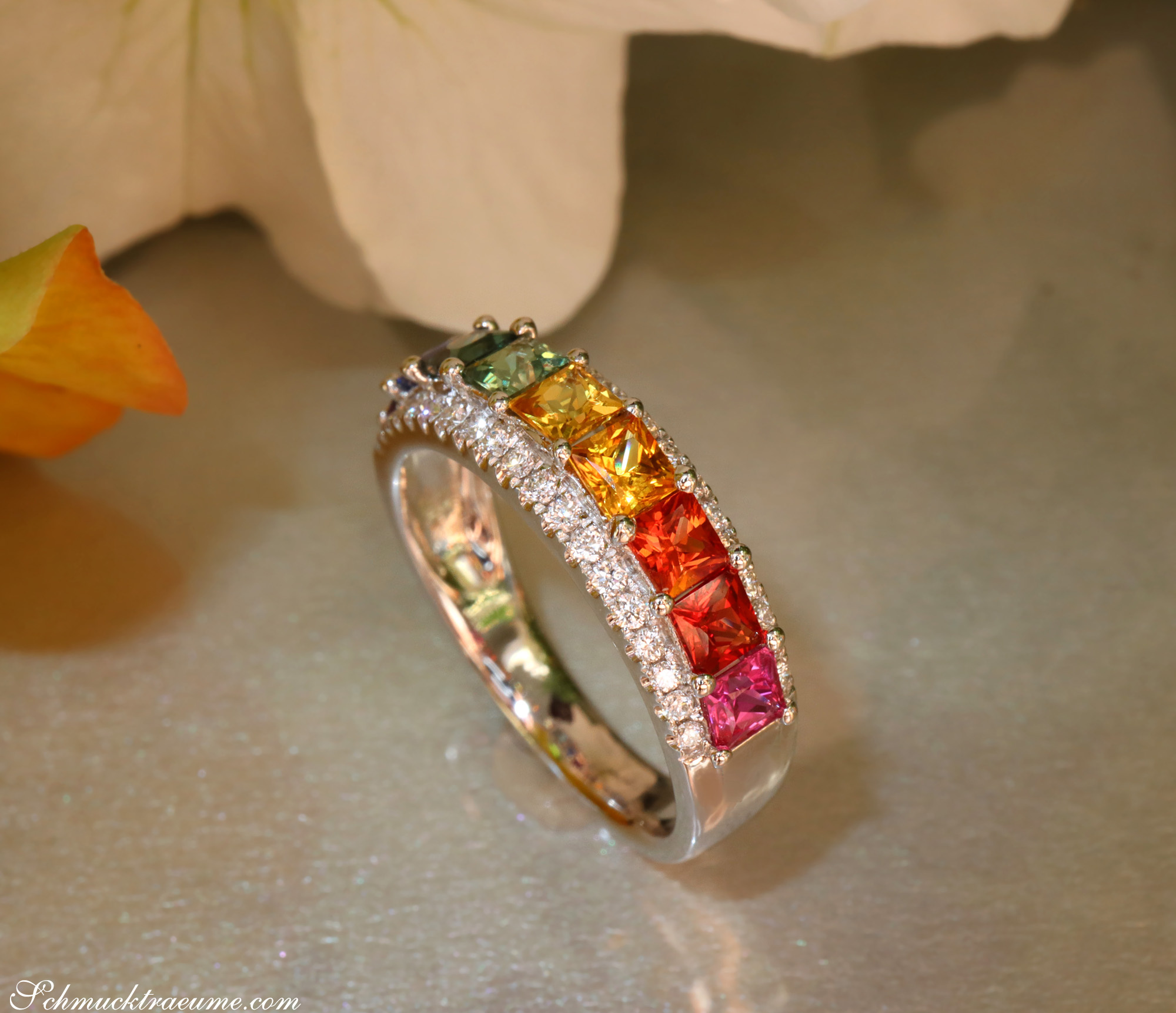 Weißgold-Ring mit Regenbogen-Saphiren und Brillanten, Detailaufnahme, Blüten im Hintergrund.
