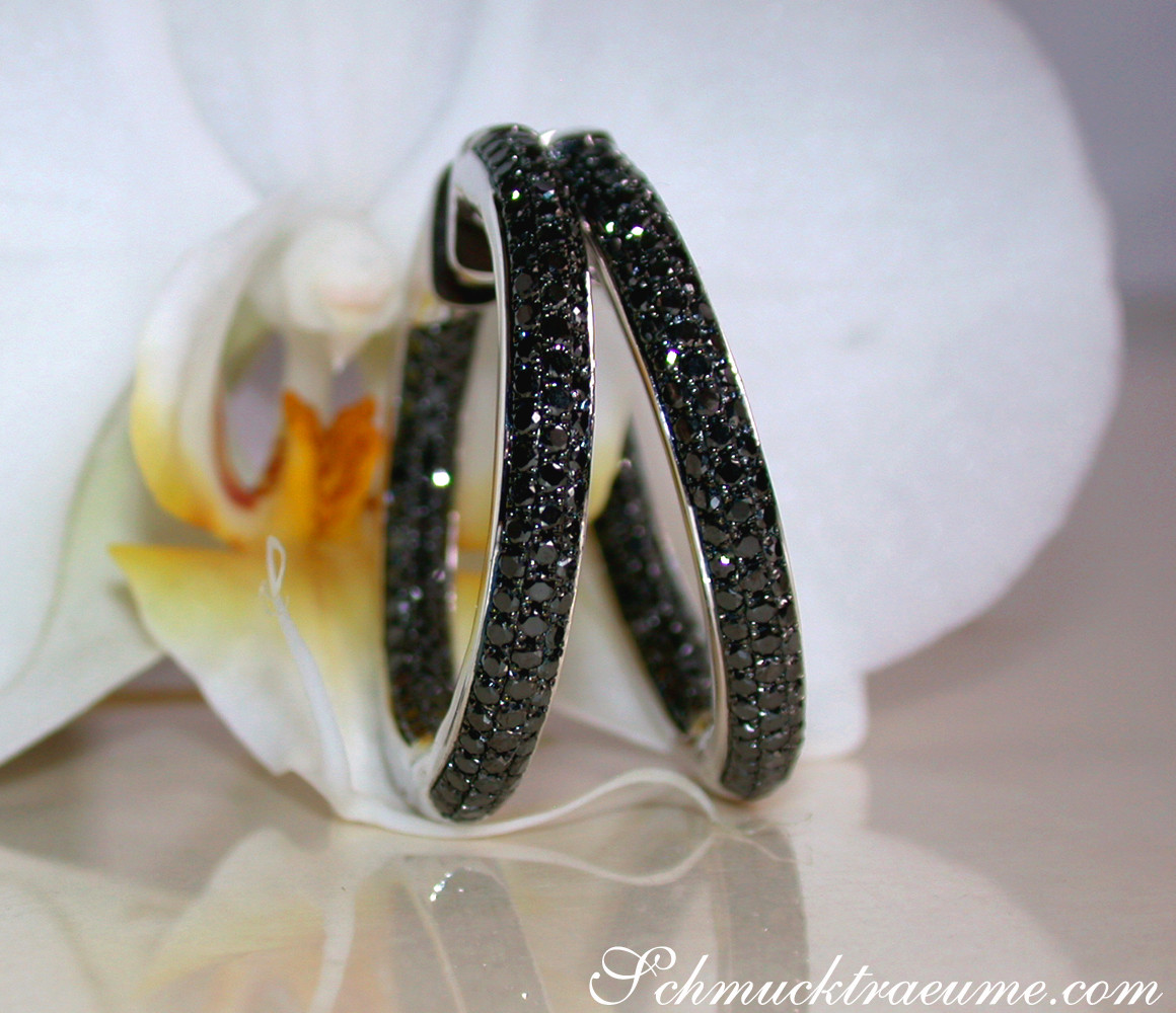 Schwarz-diamantierte Creolen auf Orchideenblüte, Detailaufnahme.