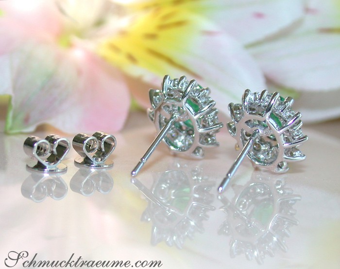 Smaragd-Ohrstecker mit Diamanten auf Silberstöcken, Hintergrund mit Blume.