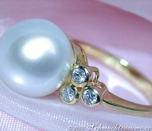 Gelbgoldring mit großen Südseeperle und Diamanten, detailreich, elegant, auf rosa Stoff liegend.