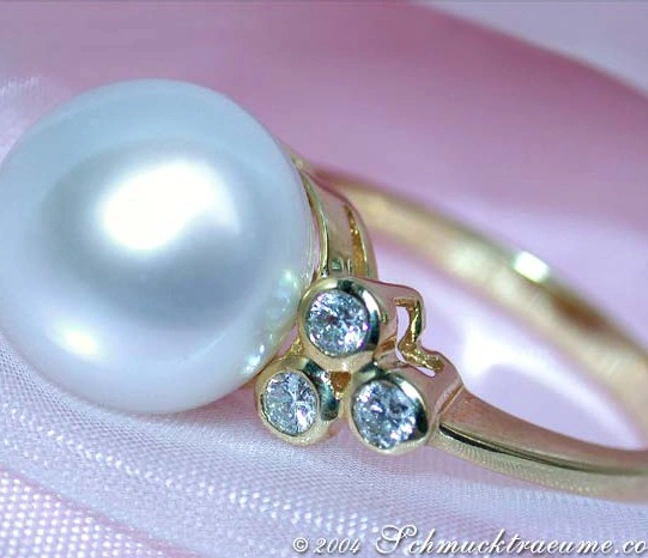 Gelbgoldring mit großen Südseeperle und Diamanten, detailreich, elegant, auf rosa Stoff liegend. Gelbgoldring mit großen Südseeperle und Diamanten, detailreich, elegant, auf rosa Stoff liegend.