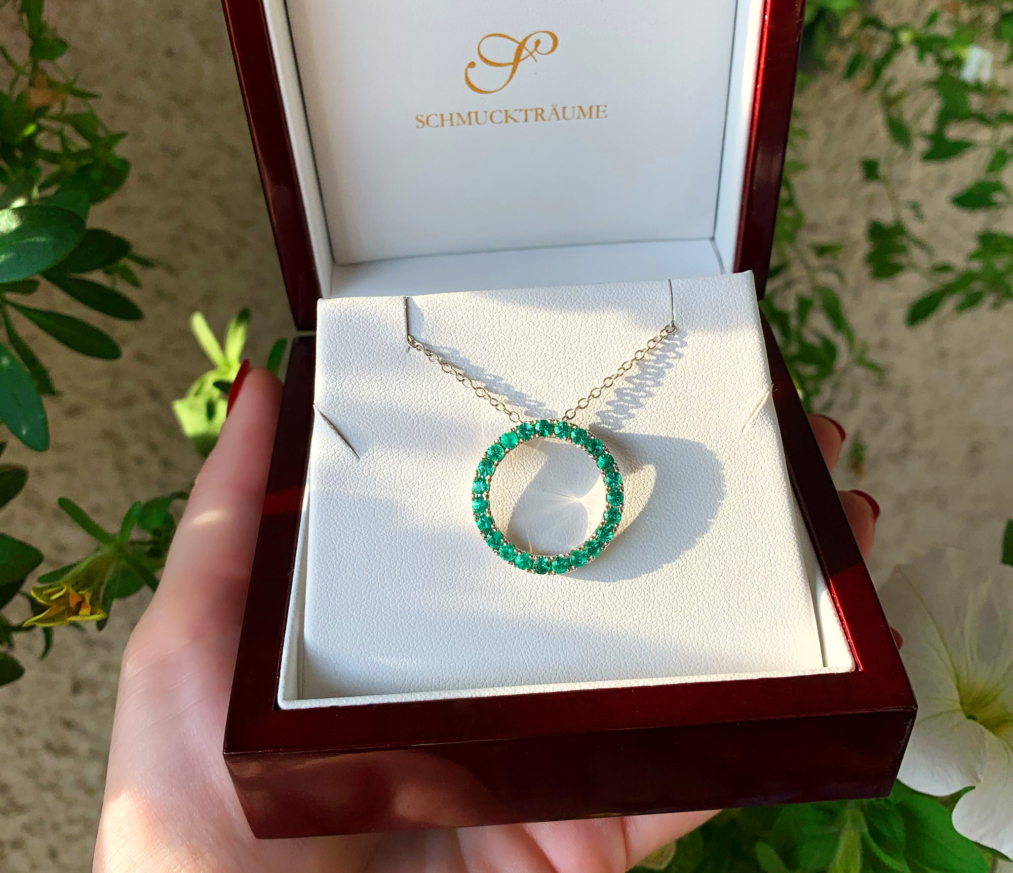 Smaragdkreisanhänger in Weißgold, Detailaufnahme, grüne Steine, zarte Kette, handgehalten.