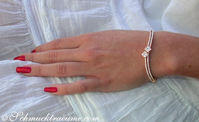 Weißgold-Armreif mit Diamanten, sanfte Kurven, rote Nägel, weißer Stoffhintergrund