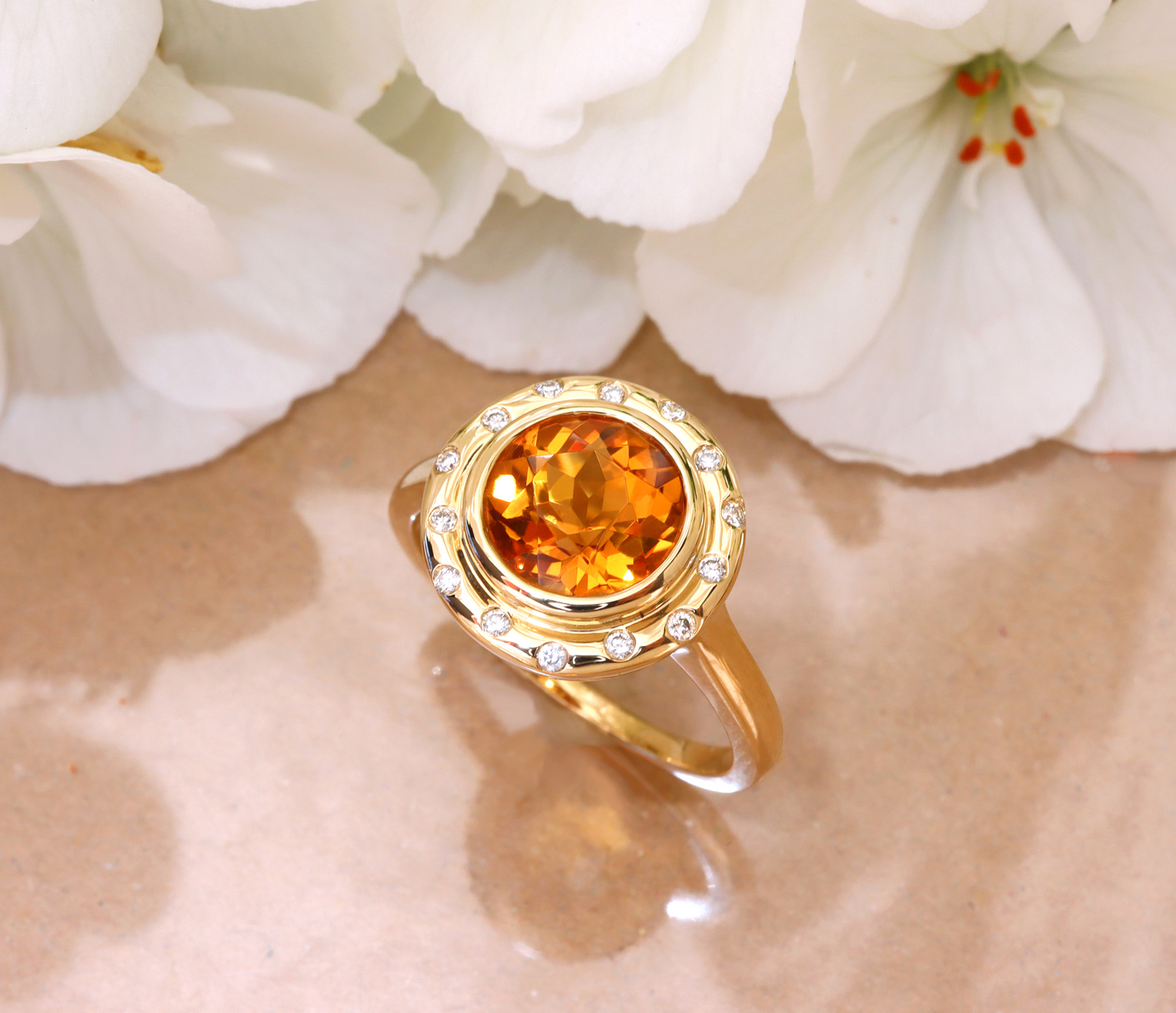 Goldener Citrin-Ring mit Diamant-Setzung, detailreich, weißer Hintergrund mit Blütenblättern.
