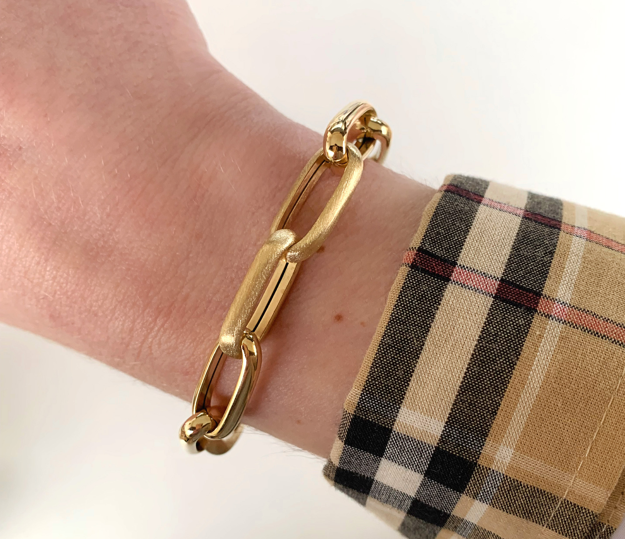 Gold-Paperclip-Armband auf Hand mit kariertem Stoffdetail