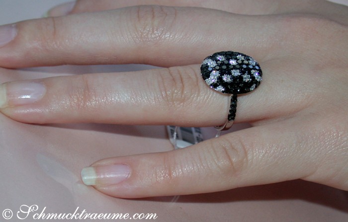 Schwarz-weißer Diamantring auf Ringfinger, Detailaufnahme mit funkelnden Steinen.