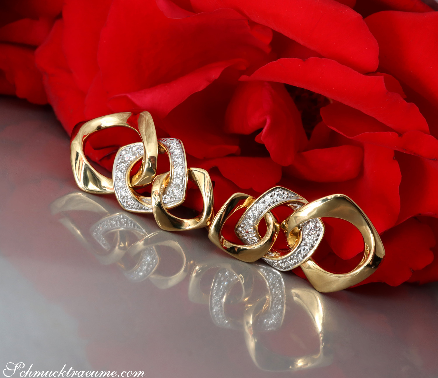 Goldene Glieder-Ohrringe mit Brillanten auf rotem Rosenblatt