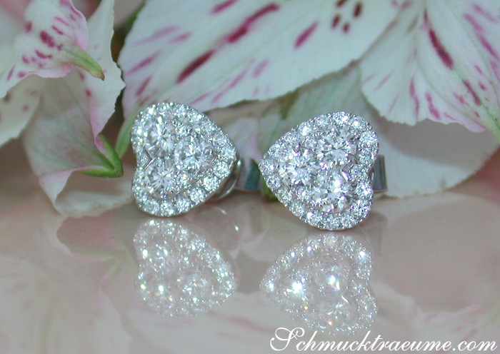 Herzformige Ohrstecker aus Weißgold 750, glitzernde Diamanten, Blumen im Hintergrund.