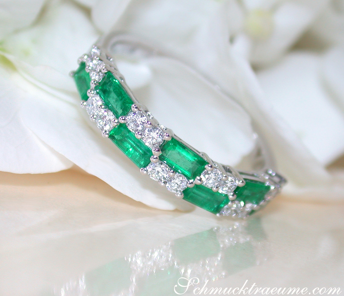 Smaragd- und Diamant-Bandring in Weißgold, detailreich, auf weißem Blütenblatt liegend.