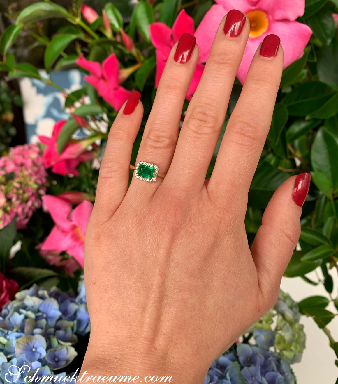 Ringszene mit Smaragd und Brillanten, Nagellack rot, Hintergrund Blumen