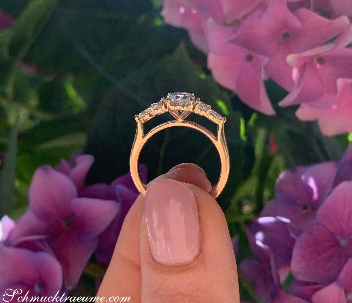 Goldener Diamant-Solitär-Ring vor rosa Blüten, Detailaufnahme.