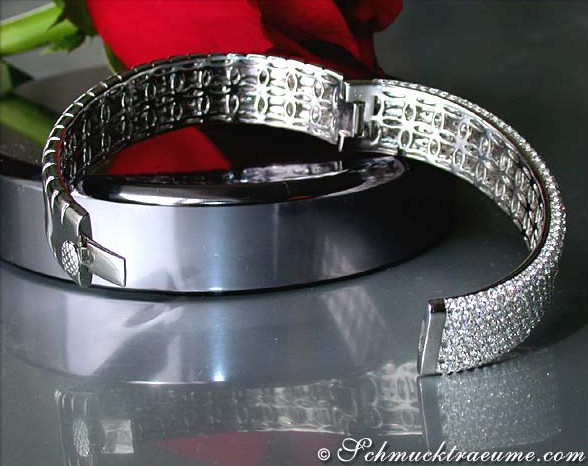 Weißgold-Armreif mit Brillanten auf glänzender Oberfläche, rote Blume im Hintergrund